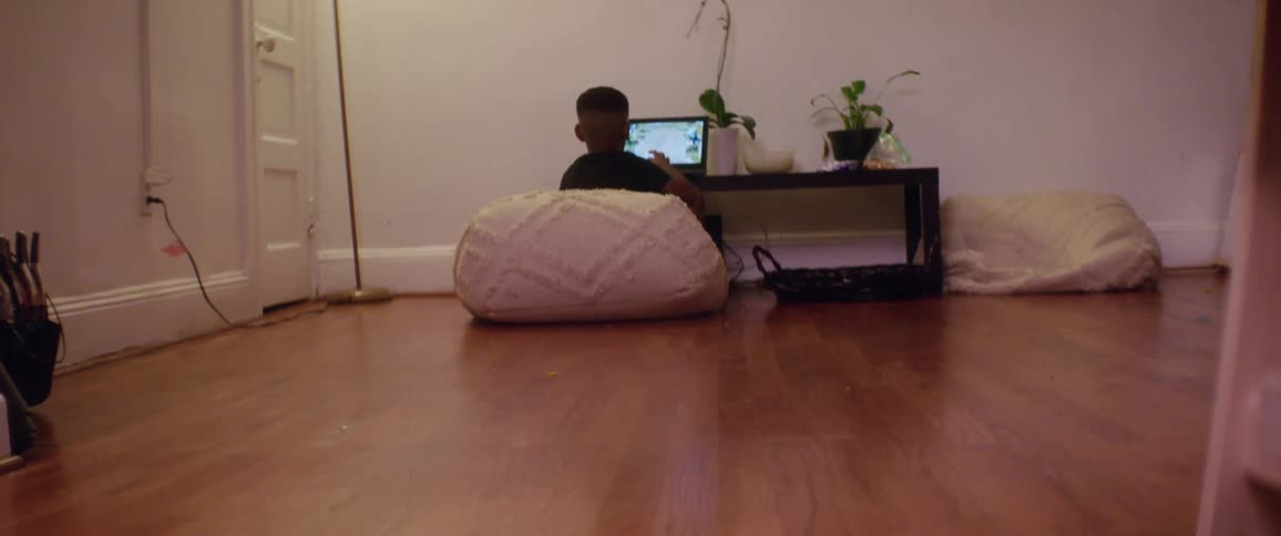 A young boy sits on a pink ottoman and uses a laptop