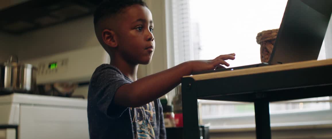 A young boy works on a laptop on a kitchen table