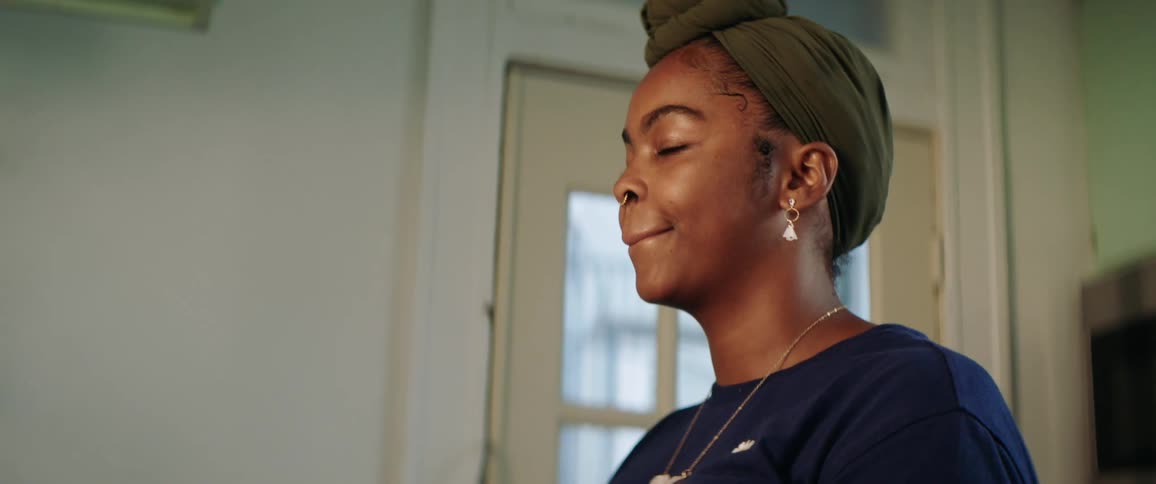 Side view of a black woman with earrings and a nose ring doing the dishes in the kitchen