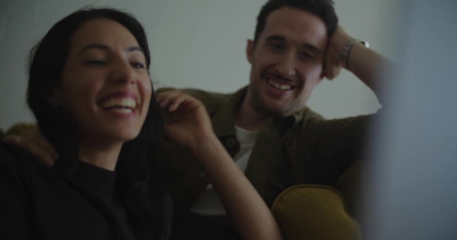 A man kisses his partner on the forehead while they cuddle on the couch