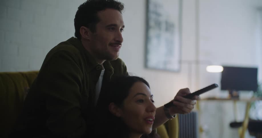 Man sits on couch behind woman sitting on floor in front of laptop as they talk
