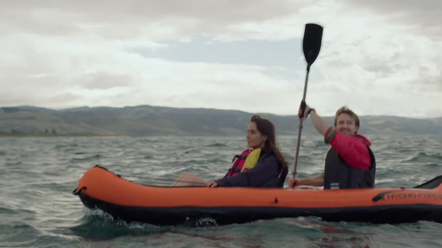 A man uses a paddle to propel an inflatable boat while traveling across a lake with a woman during the day
