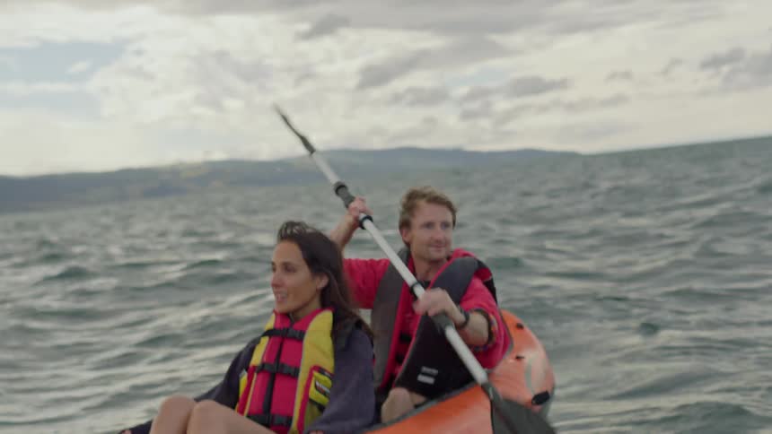 A man is looking around as he rows an inflatable boat across the water as a woman sits in front of him