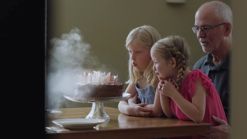 Young granddaughters help their grandpa blow out birthday candles on his birthday