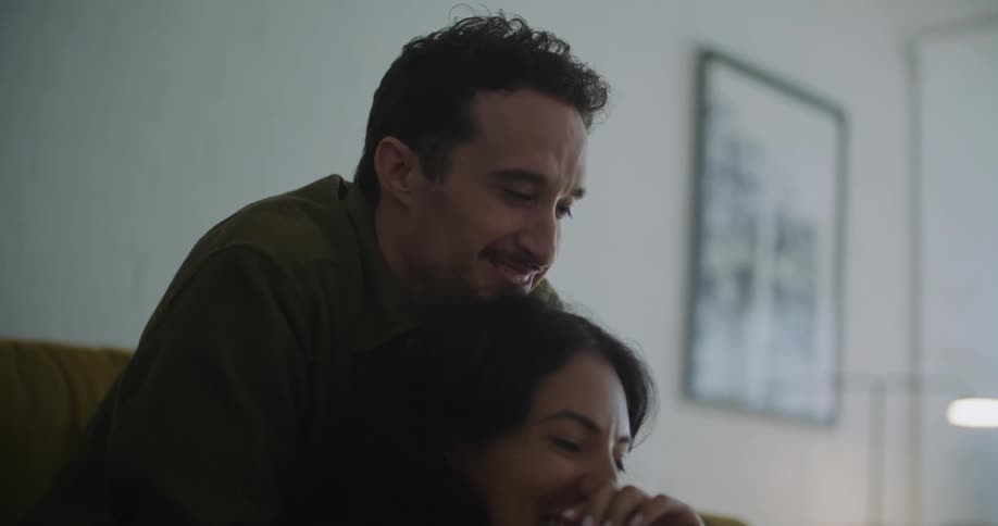 Man leans over woman as they laugh at laptop screen