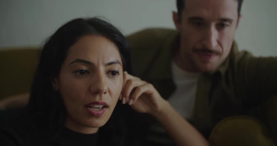 Young couple sitting on the couch talking hanging out watching something on a laptop