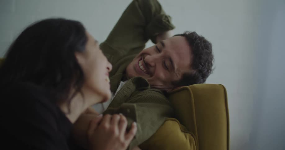 Young man and woman sitting on the couch together laughing smiling touching looking at something on the laptop