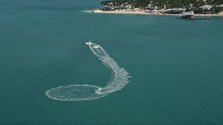 A jet skier enjoying the sunny day and driving near the shore of Key West Florida captured from a 5K aerial view during summertime