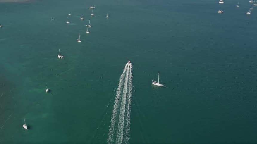 A speedboat races past a marina filled with sailboats creating waves in its wake in Key West Florida seen from an aerial during summer