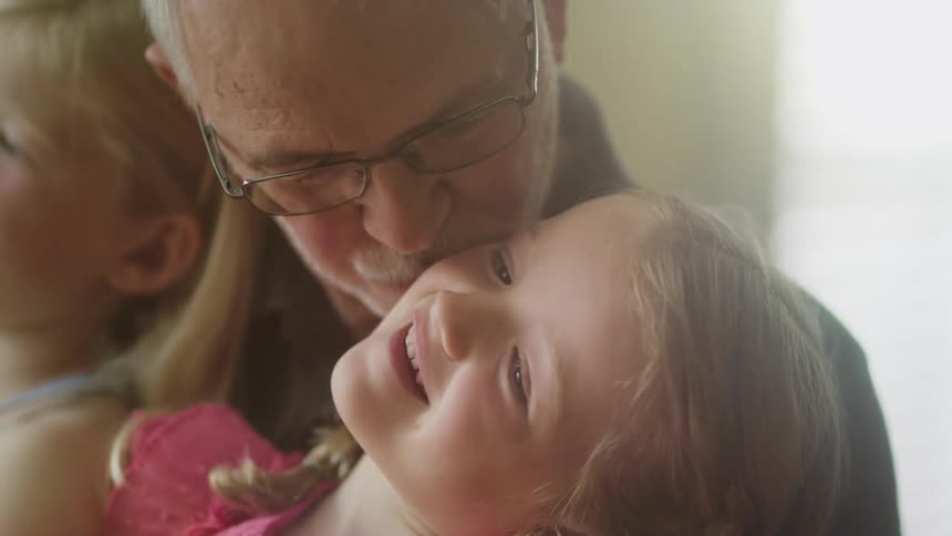 A grandfather celebrates his birthday with his two little granddaughters in a beautifully sunlit room
