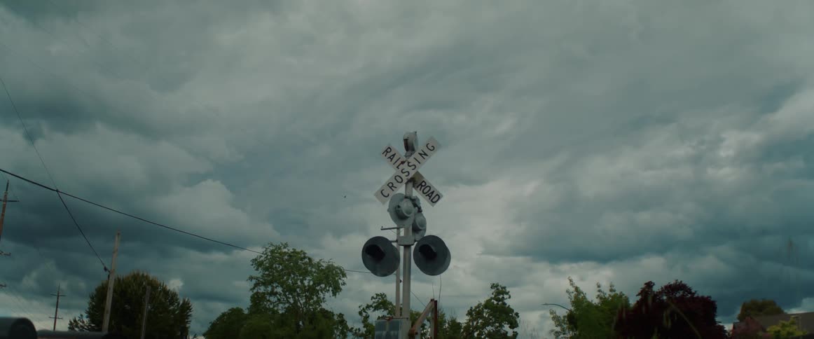 Row of mailboxes stands near railroad crossing with fenced house in the background