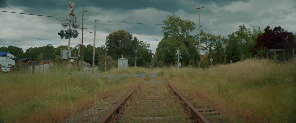 An old train track covered in grass meets a road
