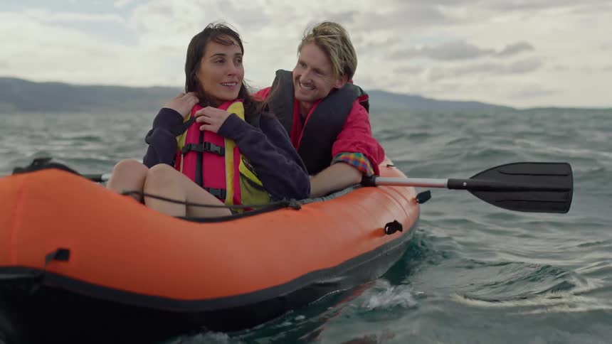 A man and woman sit in an inflated canoe far from land