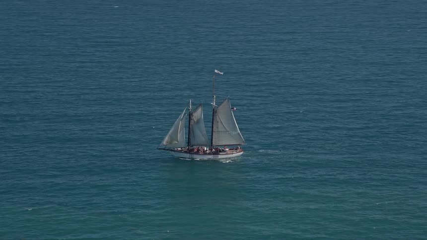 Tracking shot of a sailboat with gray sails transporting passengers across blue waters near Key West Florida during summer