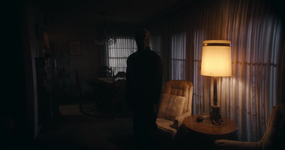 Silhouette of a person standing in front of a chair near a lamp in a dark room