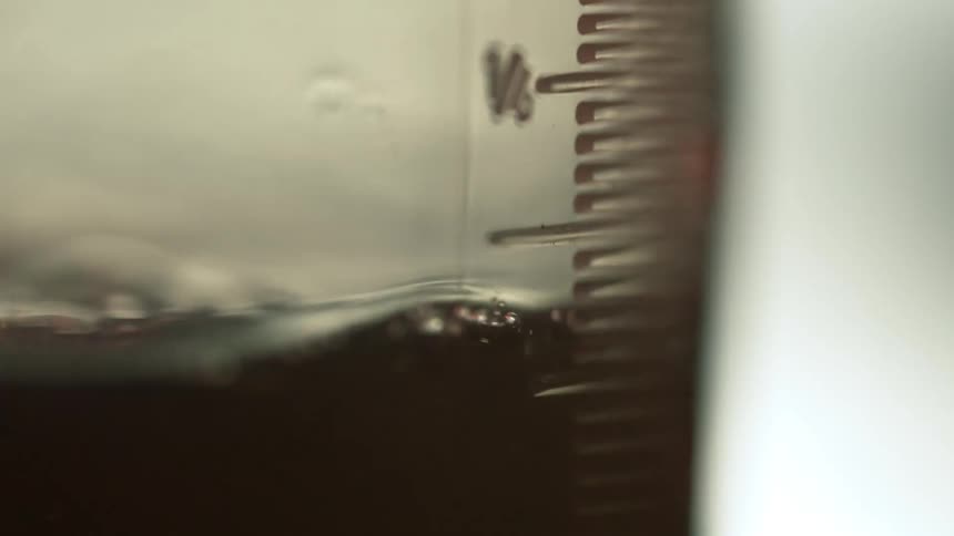 A stream of black watery liquid pours into a measuring cup