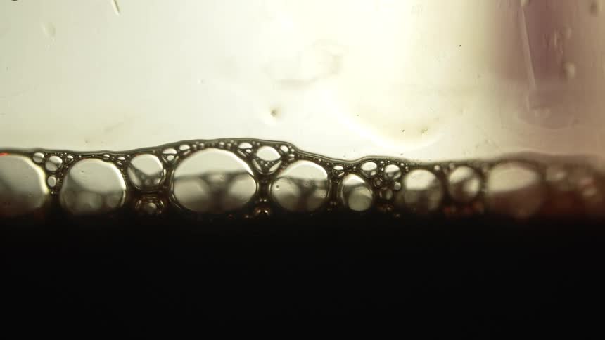 A close up of opaque black liquid is shown with bubbles popping on the surface