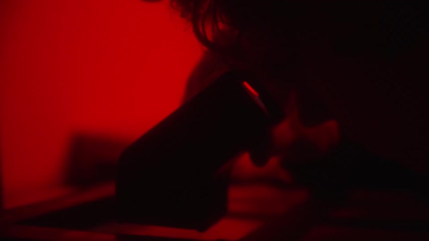 Photographer in dark room using a negative viewfinder to inspect negative film