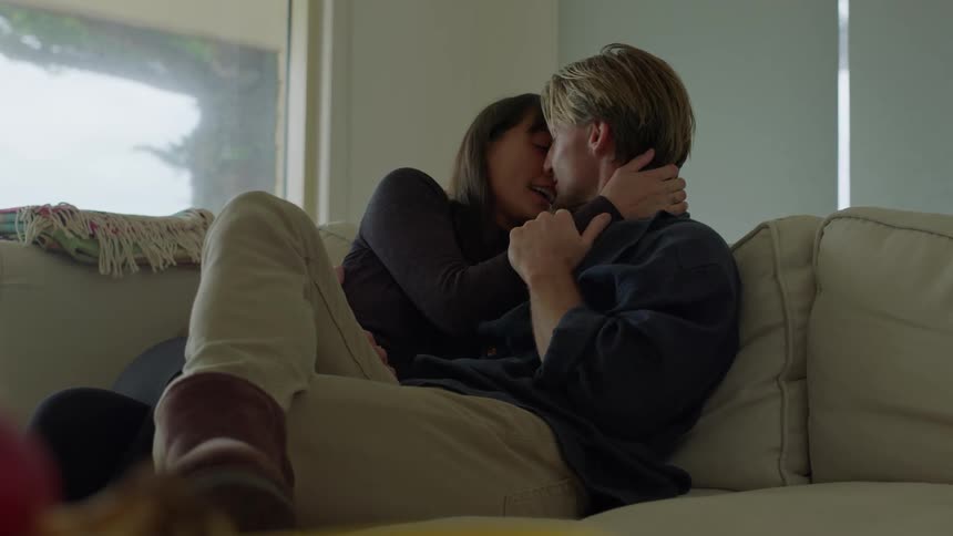 A man and woman sitting on a couch holding each other kissing and cuddling