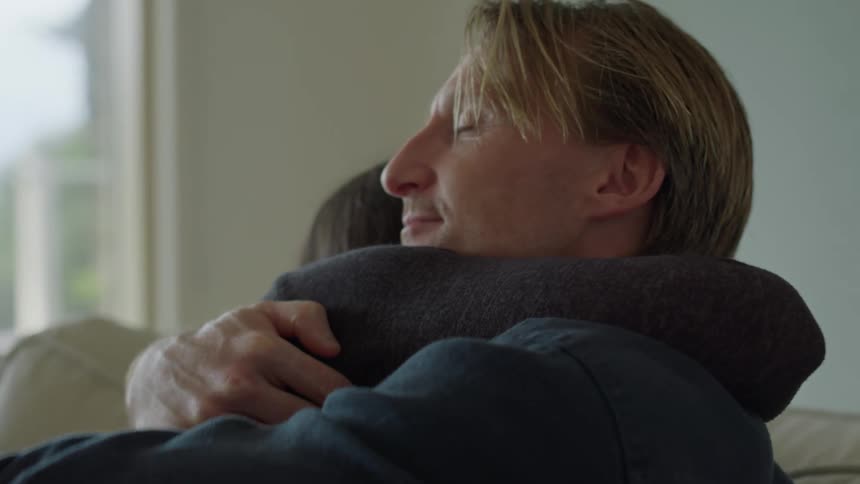 Blonde man with dark blue shirt and woman with black sweater cuddle on the sofa in the living room