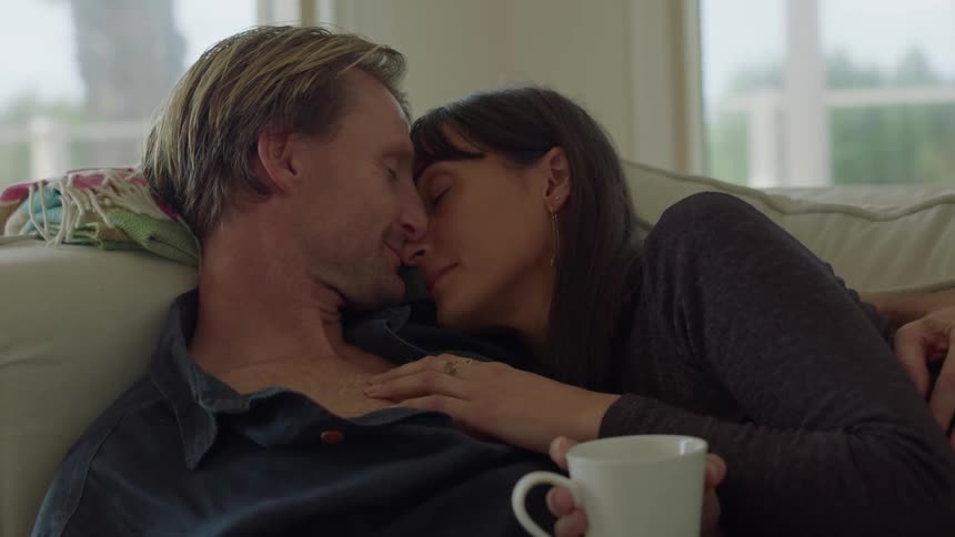 Man with blue shirt and woman in sweatshirt makes out sitting on the couch in the living room