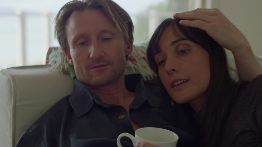 Man on woman sitting on couch together very close head on shoulder coffee and reading a magazine during the day