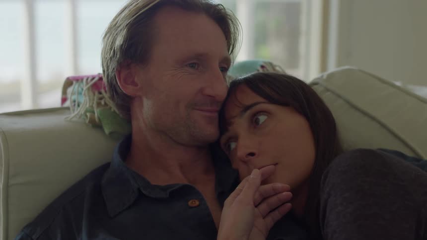 Man with dark shirt holds and kisses womans forehead sitting on the couch in the living room