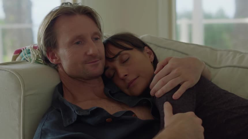 A tender and romantic moment between a man and his wife as the man lovingly holds her on the sofa