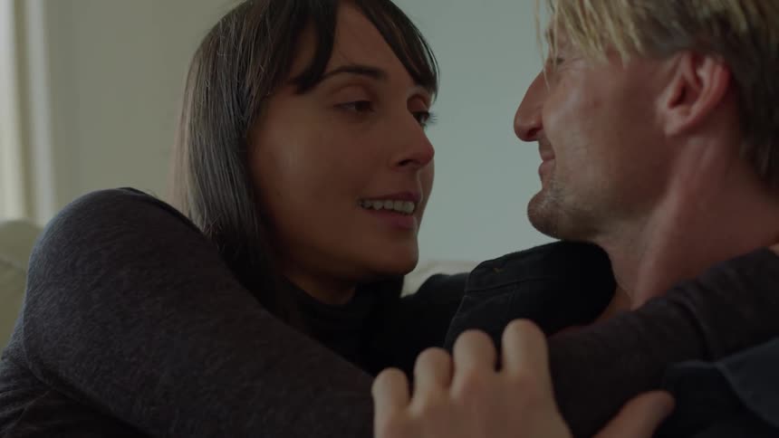 A couple kisses and holds each other while talking and laughing on a couch