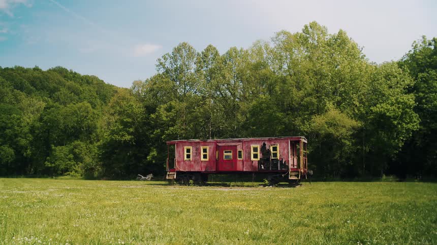 A railroad car in a field in a forest has been adapted into a small house