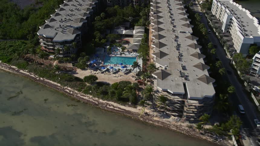 A stunning aerial footage of Key Wests coastline unveils the famous 1800 Atlantic Vacation Rentals hotels and pools along the shore as cars cruise on the highway