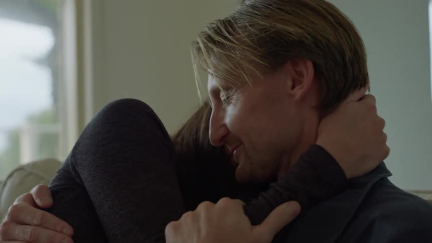 A man and woman are sitting together on the couch hugging and kissing and looking into each others eyes