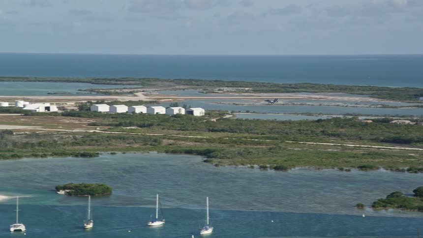 Aerial footage of an F-18 jet making a landing at Naval Air Station Key West in Florida revealing the coastline and sunny skies