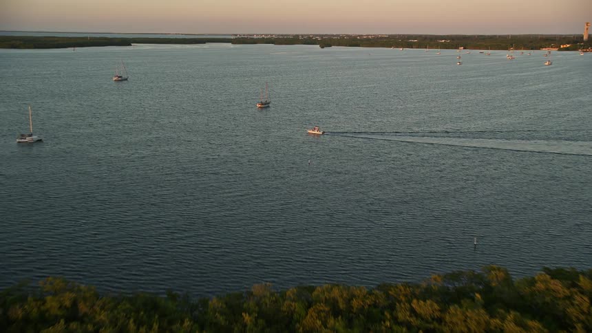 An aerial view of sailboats and a fishing boat approaching the shore as the sun sets over the mangroves in Key Largo Florida