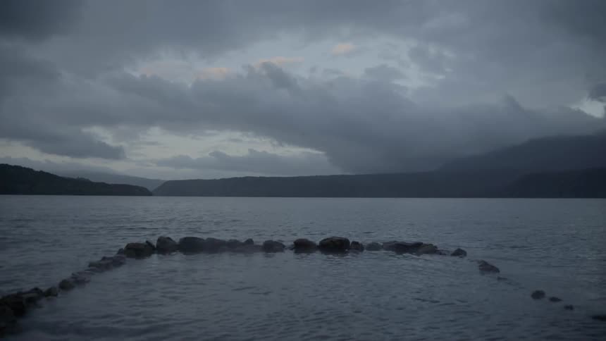 Fog blows over a lake decorated with stones at dusk