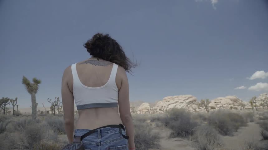 A woman walking in a desert area throws her arms out to her sides