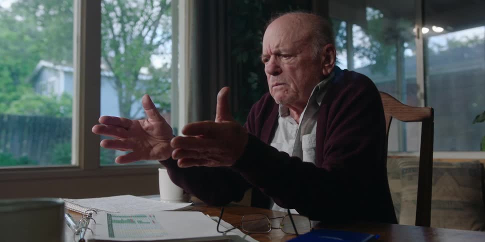 An elderly man at home yells at a business man as he shows him documents