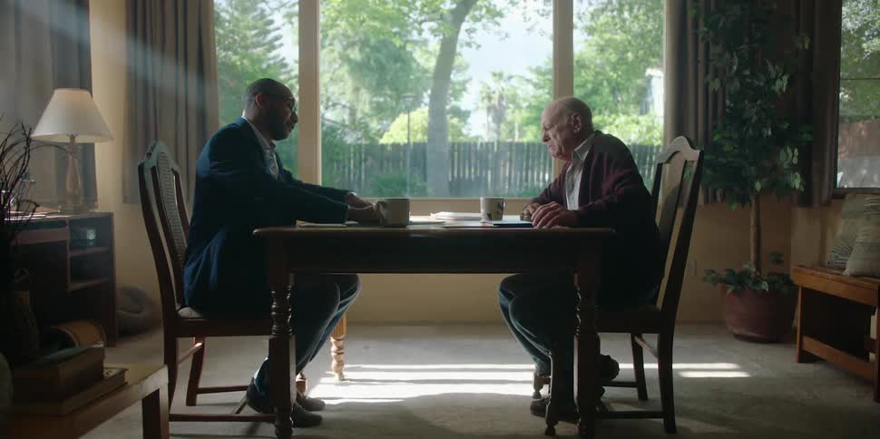 Old man and younger man sitting across each other at a dining table during the day discussing estate planning or life insurance going over documents