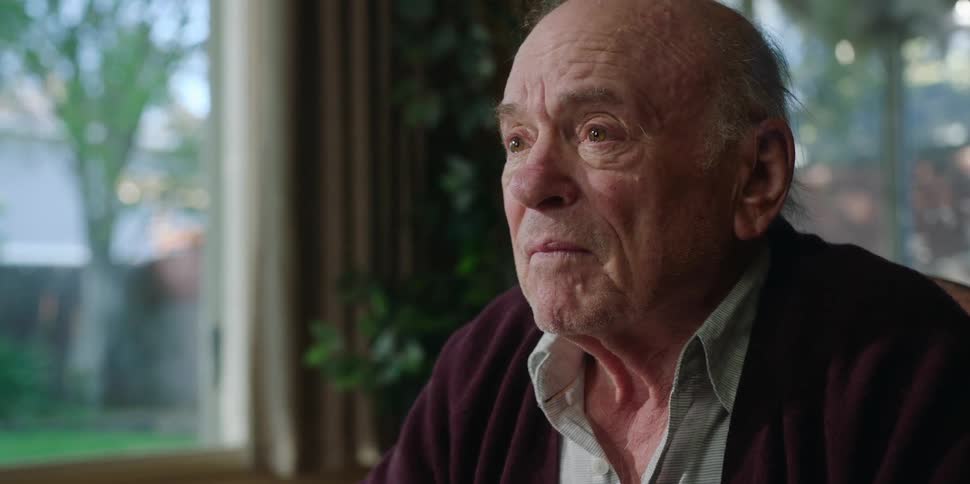 An elderly man has a conversation with another person while he gestures