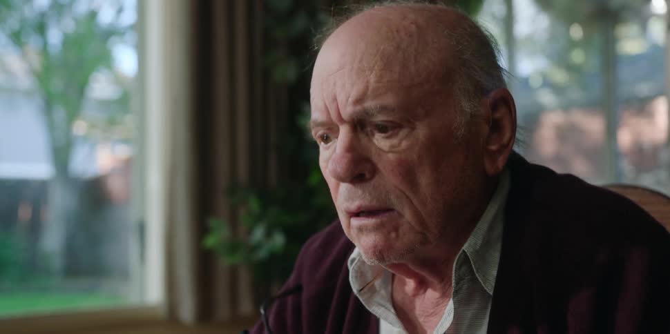 Old man sitting in chair angry with someone arguing puts on his reading glasses and gripes at someone daytime