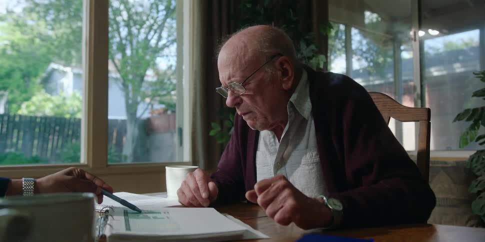 Old man sitting at dining table yelling at someone across from him about paperwork very hostile puts on reading glasses and looks continues to shout daytime
