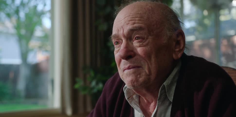 An elderly man at home tears up as he talks