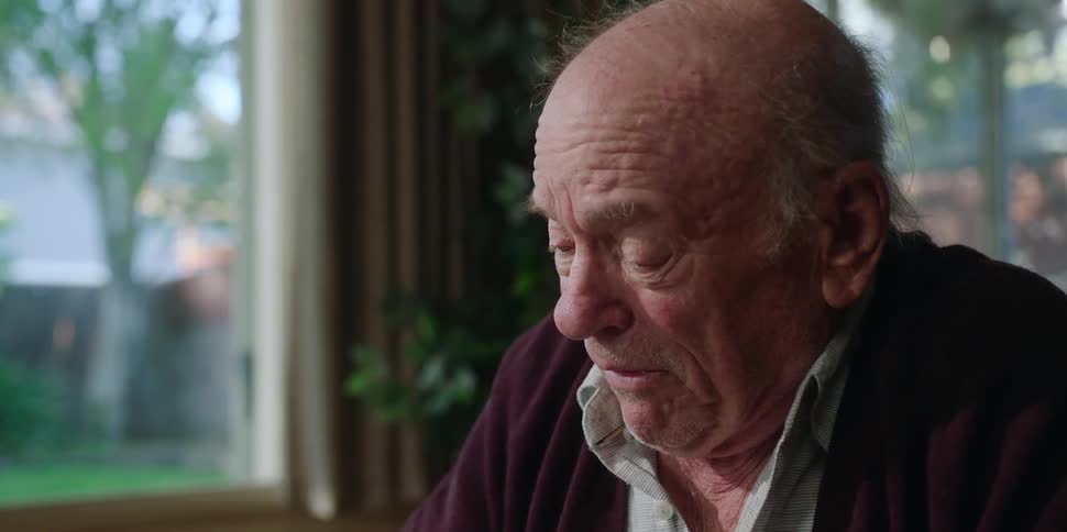 An elderly man is sitting down talking to another person and becoming very emotional as he speaks