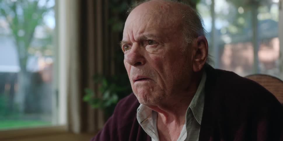 An elderly man has a look of confusion on his face before putting on glasses to read