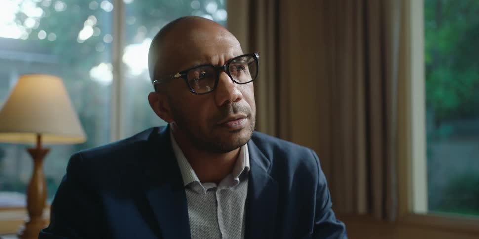 A black man wearing glasses talks to someone and moves his hands