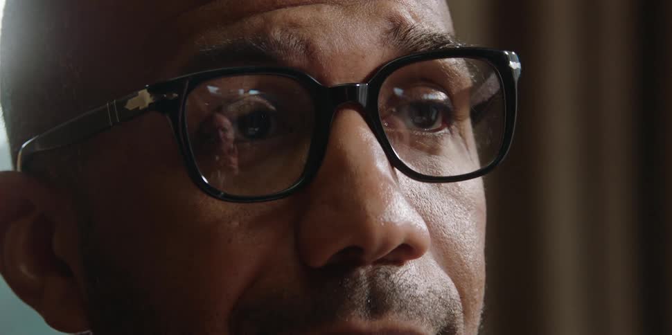 A young man nods his head with the reflection of an elderly man in his glasses