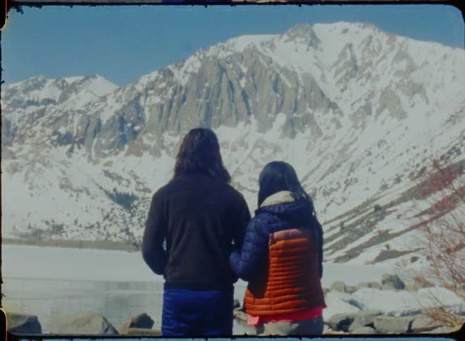 A woman rests her head on her partners shoulder while looking at a snow covered mountain