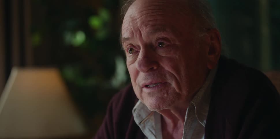 Old man sitting in chair at home at nighttime having a conversation with someone seems discouraged and doubtful