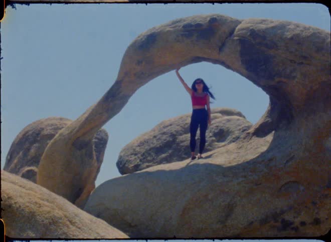 An old film of a young woman under an rock arch waiting to get her picture taken