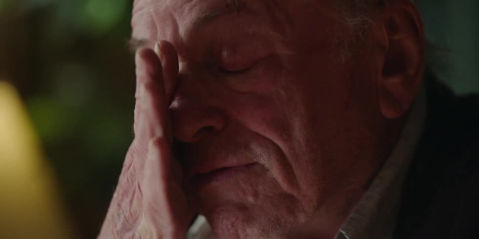 An elderly man wipes tears from his eyes as he talks